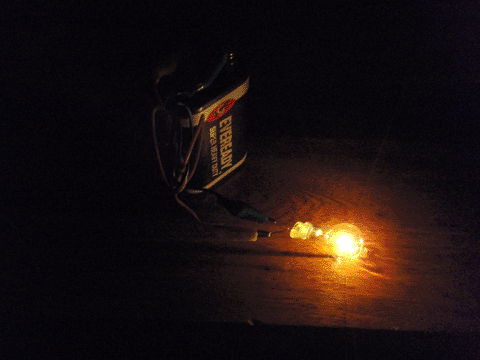 Light bulb, lit, on a table in a dark room